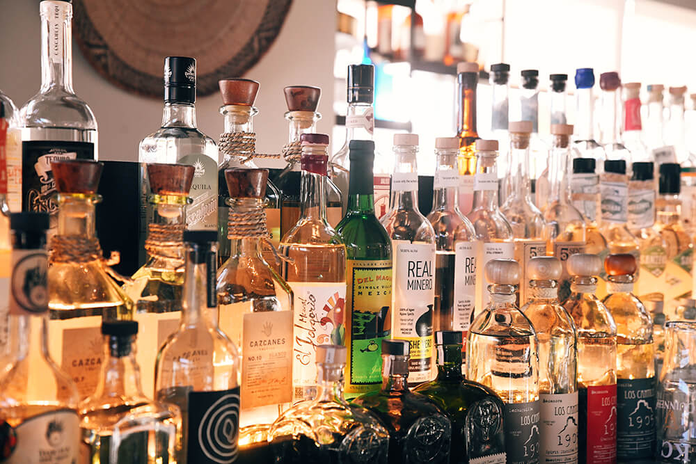 Artisan tequila and mezcal bottles lined on a backlit bar